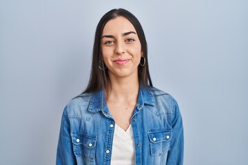 Hispanic woman standing over blue background relaxed with serious expression on face. simple and...