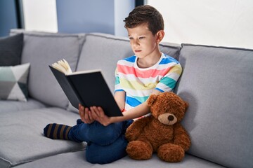 Young caucasian kid sitting on the sofa reading a book relaxed with serious expression on face. simple and natural looking at the camera.