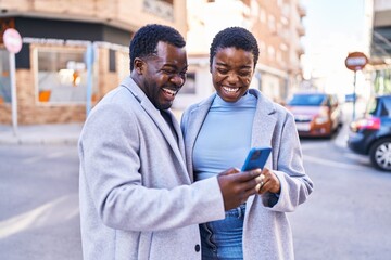 Man and woman couple standing together using smartphone at street