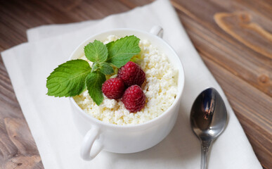 Cottage cheese with mint and raspberries in a white bowl over wooden baclground.
