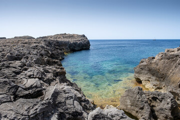 Fototapeta na wymiar a small rocky cove on the coast of Menorca, with crystal clear blue waters, on a clear summer day, Es Grau, Menorca, Balearic Islands, Spain