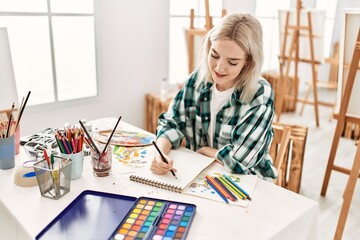 Young artist student girl smiling happy painting sitting on desk at art studio.