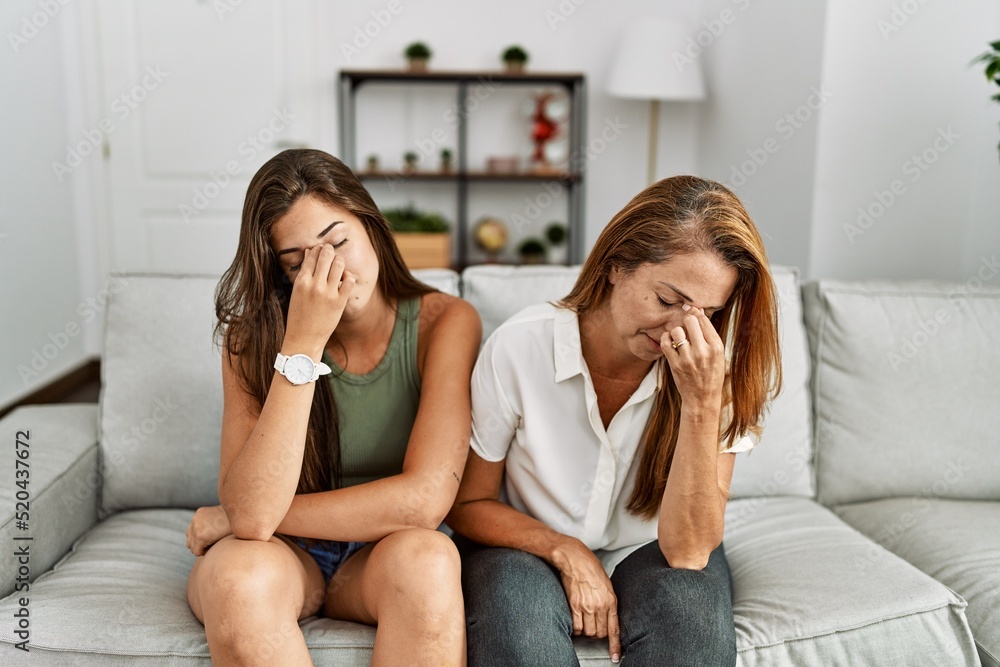 Poster Mother and daughter together sitting on the sofa at home tired rubbing nose and eyes feeling fatigue and headache. stress and frustration concept.