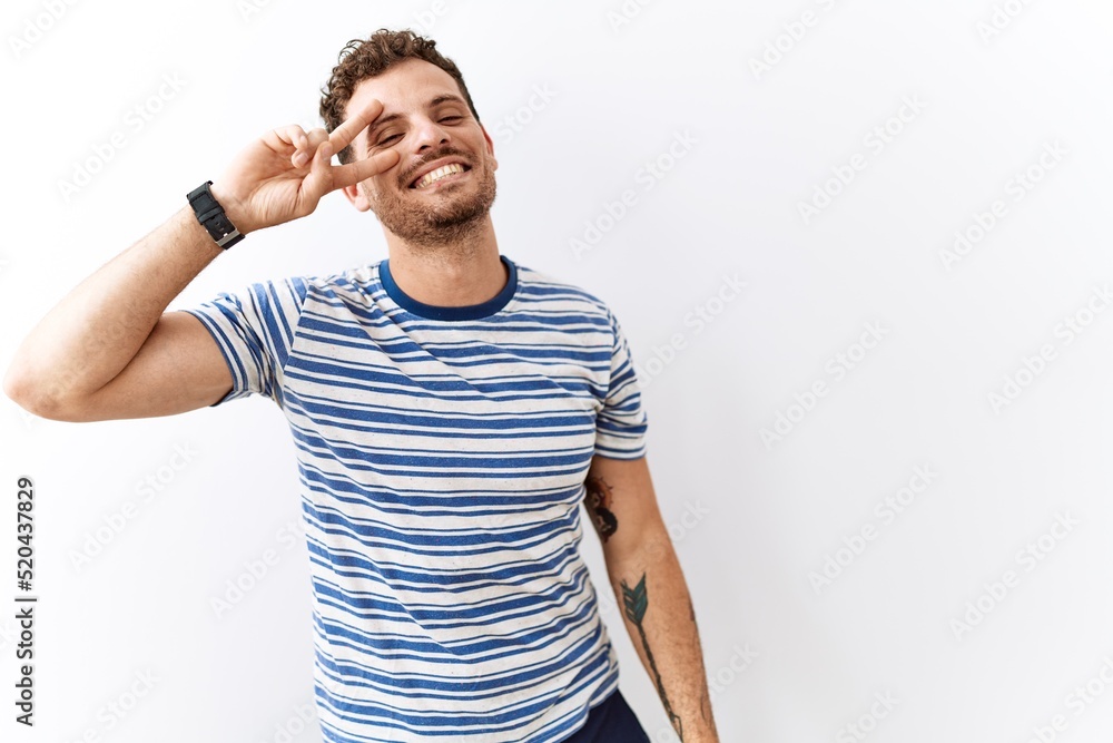 Poster Handsome young man standing over isolated background doing peace symbol with fingers over face, smiling cheerful showing victory