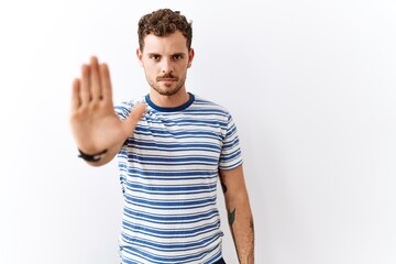 Handsome young man standing over isolated background doing stop sing with palm of the hand. warning...