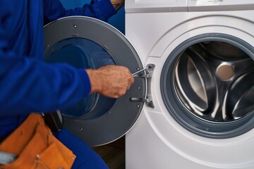 Young hispanic man technician repairing washing machine at laundry room