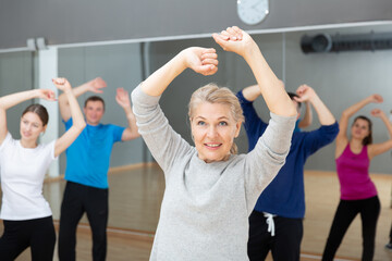 Portrait of sporty smiling mature woman practicing vigorous lindy hop movements in dance class