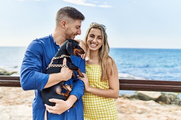 Fototapeta na wymiar Young caucasian couple smiling happy and hugging with dog at the beach.