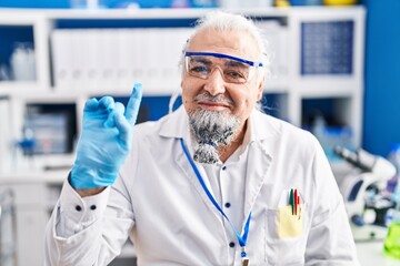 Middle age man with grey hair working at scientist laboratory smiling with an idea or question pointing finger with happy face, number one
