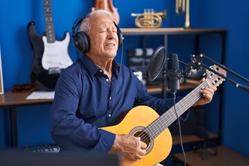 Senior grey-haired man musician singing song playing guitar at music studio