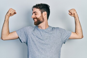 Caucasian man with beard wearing casual grey t shirt showing arms muscles smiling proud. fitness concept.