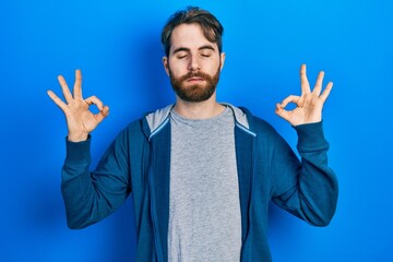 Naklejka premium Caucasian man with beard wearing casual sweatshirt relax and smiling with eyes closed doing meditation gesture with fingers. yoga concept.
