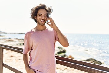 Fototapeta na wymiar Young hispanic man smiling happy talking on the smartphone standing at the beach.