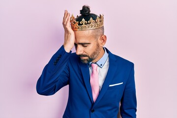 Young hispanic man wearing business clothes and king crown surprised with hand on head for mistake,...