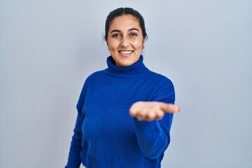 Young hispanic woman standing over isolated background smiling cheerful offering palm hand giving assistance and acceptance.