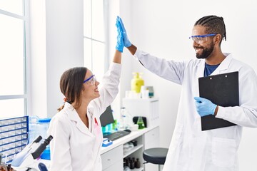 Man and woman scientist partners holding clipboard high five raised up hands at laboratory