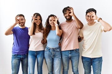 Group of young people standing together over isolated background doing ok gesture with hand smiling, eye looking through fingers with happy face.