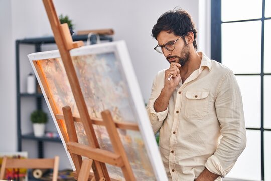 Young hispanic man artist drawing with serious expression at art studio