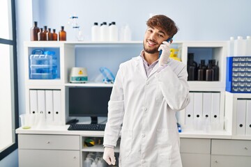 Young arab man scientist smiling confident talking on smartphone at laboratory