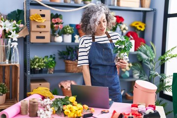 Middle age grey-haired woman florist using laptop holding plant at florist