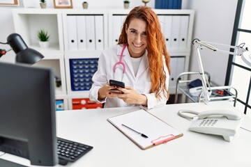 Obraz na płótnie Canvas Young redhead woman wearing doctor uniform using smartphone at hospital