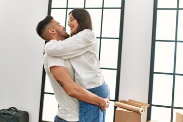 Young hispanic man holding woman in arms and hugging at new home.