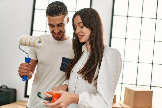 Young hispanic couple painting using paint roller at new home.