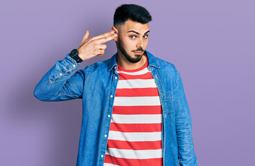 Young hispanic man with beard wearing casual denim jacket shooting and killing oneself pointing...