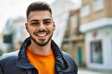 Fototapeta premium Handsome hispanic man with beard smiling happy and confident at the city wearing winter coat