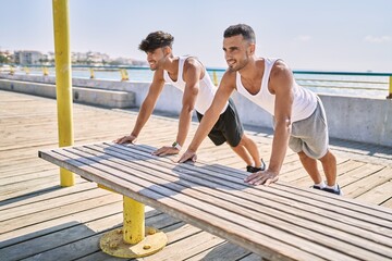 Two hispanic men couple smiling confident stretching at seaside