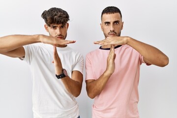 Young gay couple standing over isolated background doing time out gesture with hands, frustrated and serious face