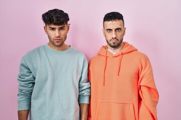 Young hispanic gay couple standing over pink background skeptic and nervous, frowning upset because...