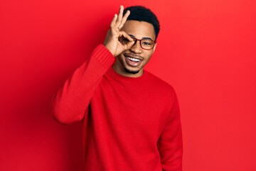 Young african american man wearing casual clothes and glasses doing ok gesture with hand smiling, eye looking through fingers with happy face.