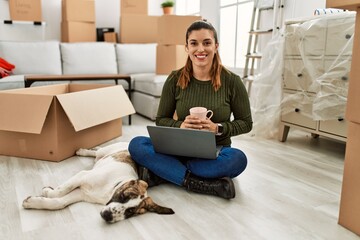 Young woman using laptop and drinking coffee sitting on floor with dog at home