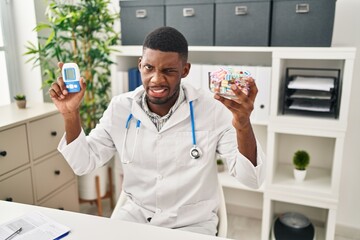 African american doctor man using glucose meter clueless and confused expression. doubt concept.