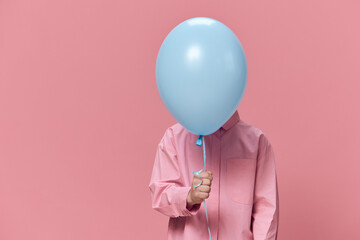 a cute, funny boy of school age stands on a pink background in pink clothes and funny hides his...
