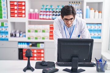 Young hispanic man pharmacist smiling confident using computer at pharmacy