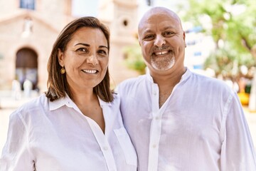 Middle age hispanic couple of husband and wife together on a sunny day outdoors. Smiling happy in love hugging at the city