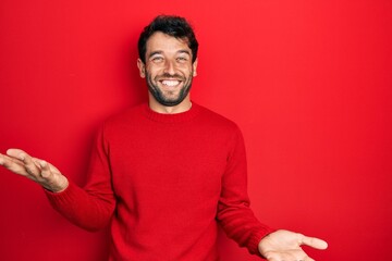 Handsome man with beard wearing casual red sweater smiling cheerful with open arms as friendly...