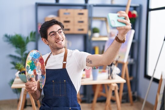 Young hispanic man artist smiling confident make selfie by smartphone at art studio