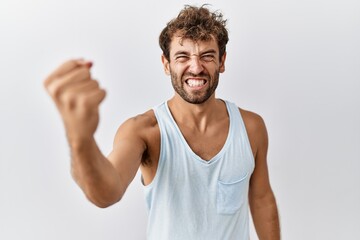 Young handsome man standing over isolated background angry and mad raising fist frustrated and...