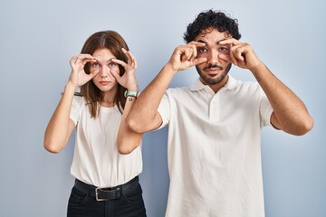 Young couple wearing casual clothes standing together trying to open eyes with fingers, sleepy and tired for morning fatigue