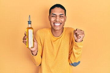 Young african american guy holding olive oil can screaming proud, celebrating victory and success...