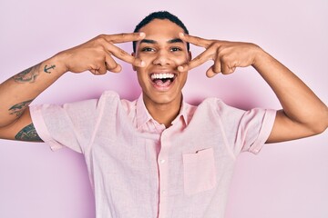 Young african american guy doing victory sign and peace gesture celebrating crazy and amazed for...
