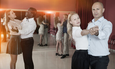Young positive people learning to dance waltz together in dancing class