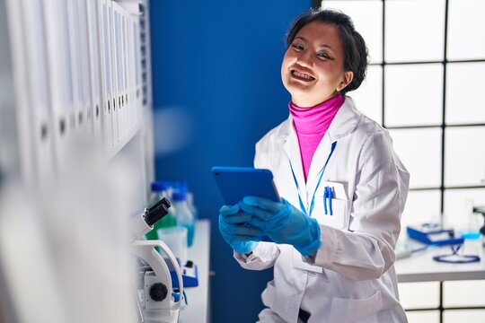 Young chinese woman scientist smiling confident using touchpad at laboratory