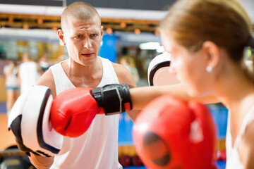 Young woman in gloves exercising hook punches with trainer who wearing focus mitts.