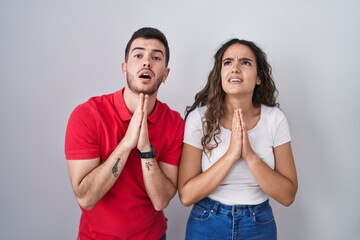 Naklejka premium Young hispanic couple standing over isolated background begging and praying with hands together with hope expression on face very emotional and worried. begging.