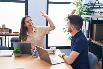 Young hispanic couple business workers high five with hands raised up working at office