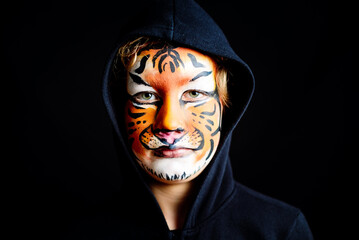 Mysterious look of a child with feline character, painted the face of a dangerous, serious tiger, isolated on black background.